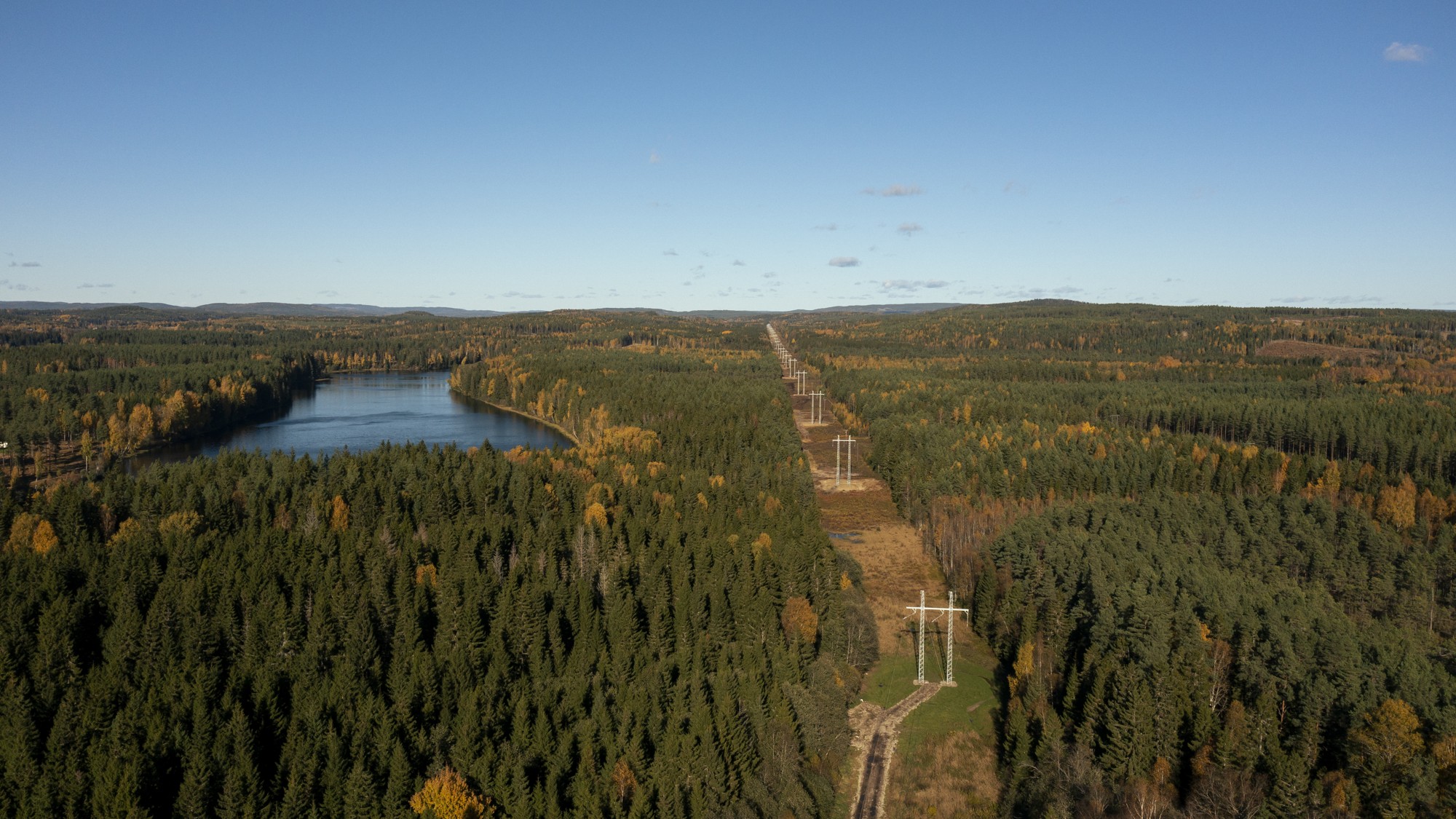 Flygbild över en kraftledningsgata som löper genom ett skogslandskap med en sjö intill.