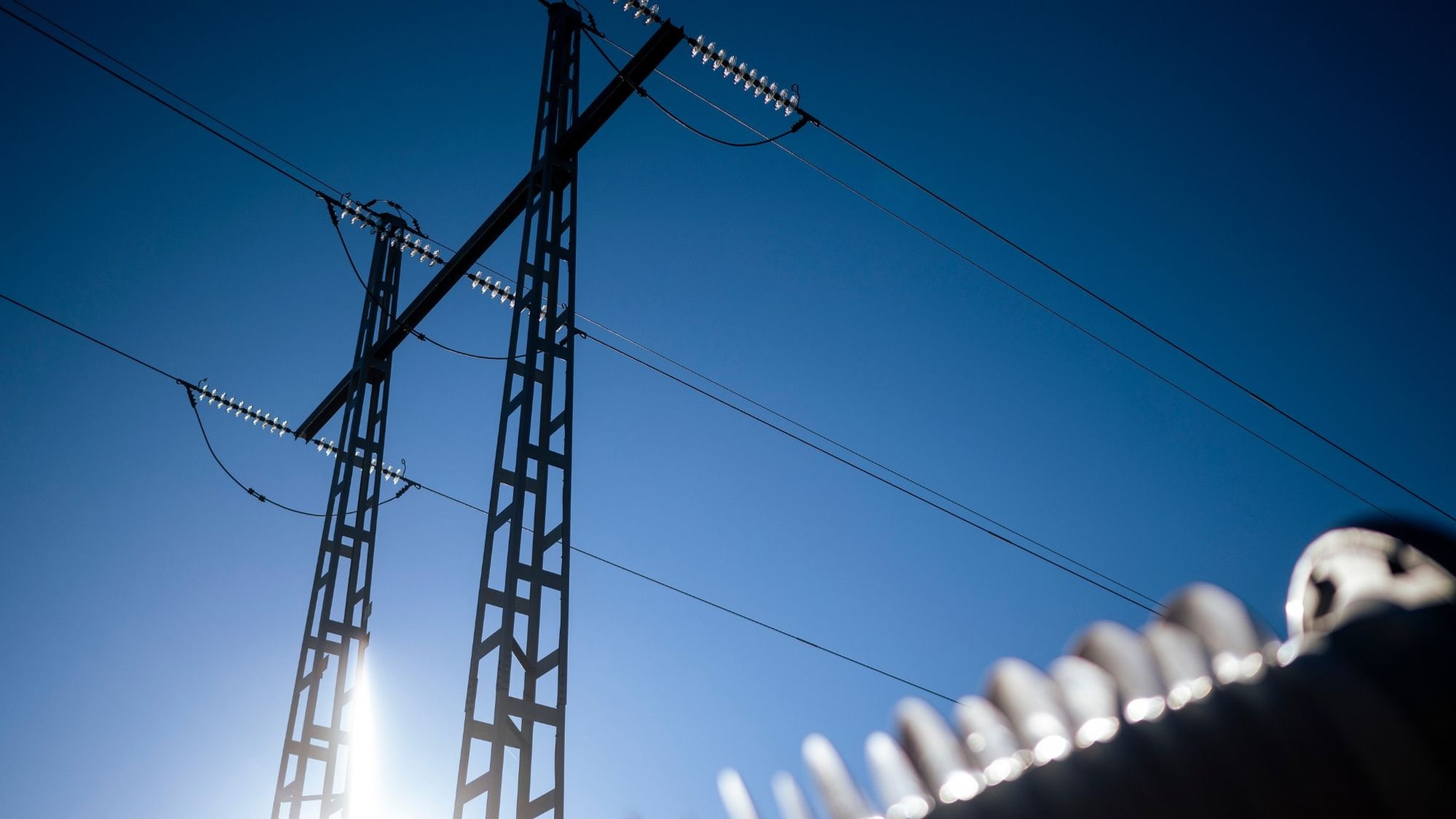 Solen skiner bakom kraftledningarna.