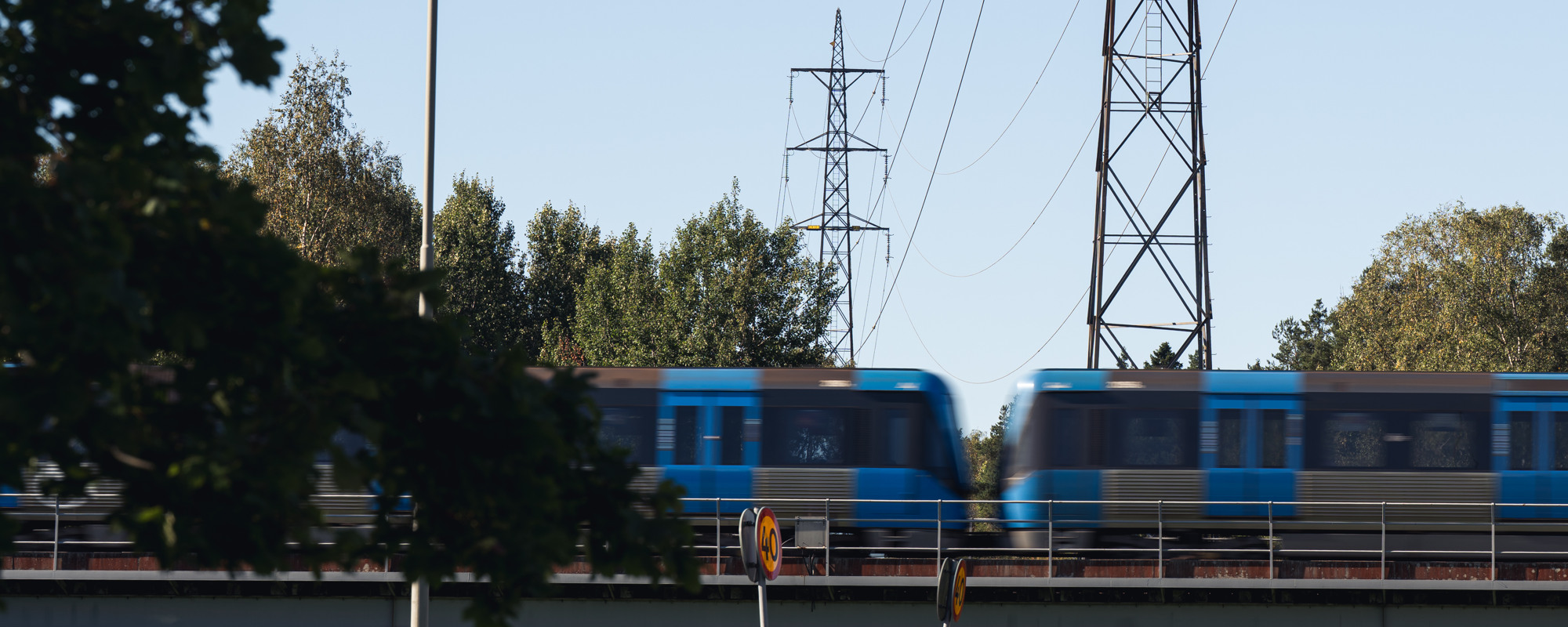 Ett tunnelbanetåg som färdas på järnvägsspår med elstolpar i bakgrunden.
