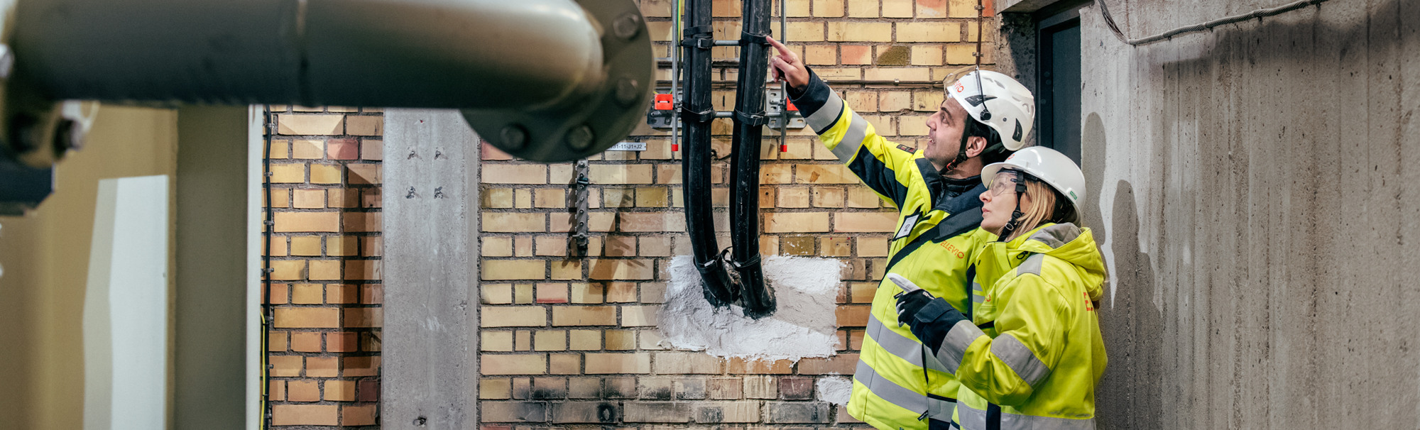 En man och en kvinna står framför en tegelvägg i en fördelningsstation.