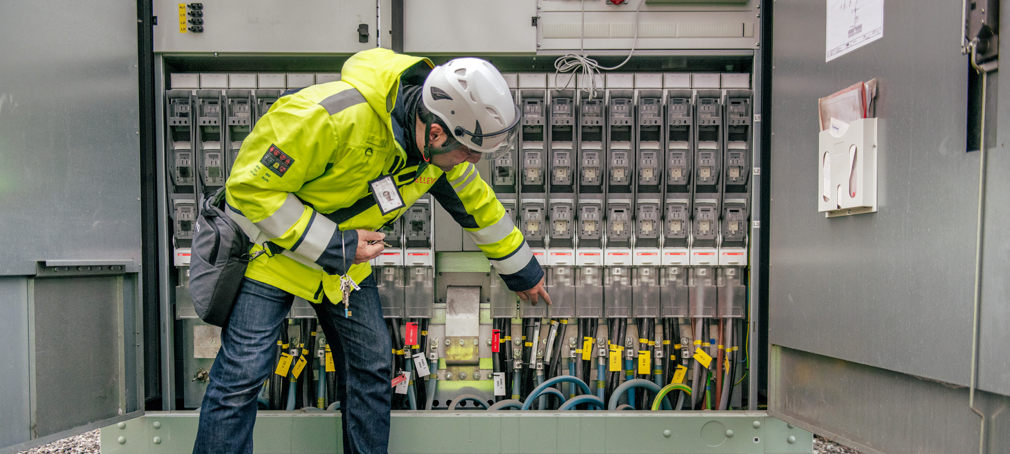 En man i skyddsväst och skyddshjälm arbetar med en nätstation