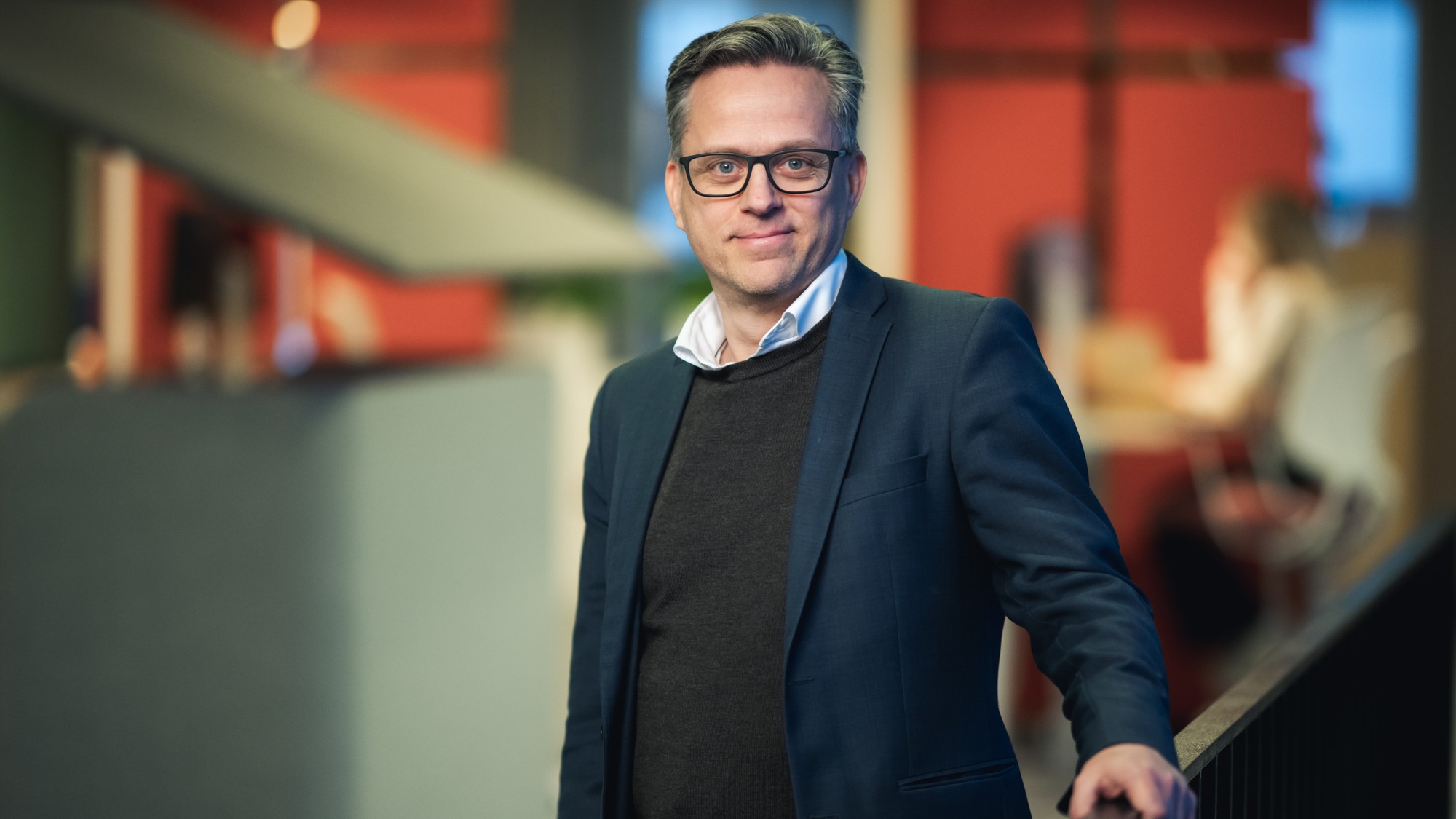 En man i kostym och glas&ouml;gon st&aring;r p&aring; en trappa.